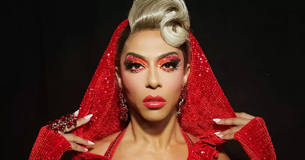 Drag queen Shagela posing for a photo wearing a red dress and cowl.
