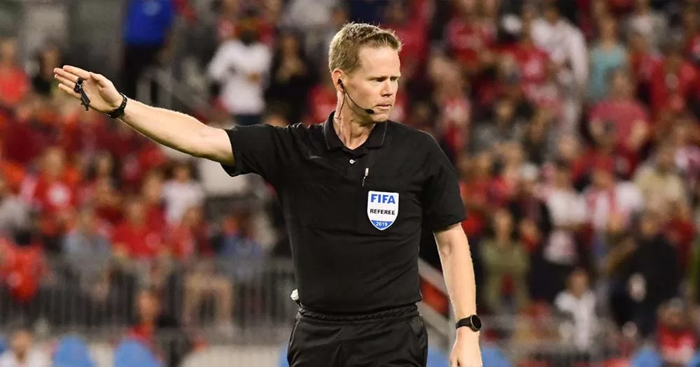 Photo of referee Drew Fischer raising right arm, he stopped the CONCACAF game due to homophobic chants