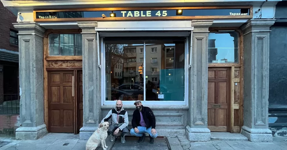 The image shows the front of new Dublin tapas bar Table 45. crouched in front of the building are two men with a gold labrador dog. Both men have black beards and one is resting his arm on the dog.