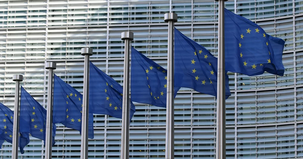 This article is about EU systems for asylum seekers. The image shows EU flags at the European Commission Berlaymont building.