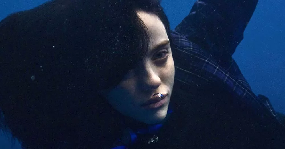 Photo of Billie Eilish floating in deep blue water as part of the announcement of her third album