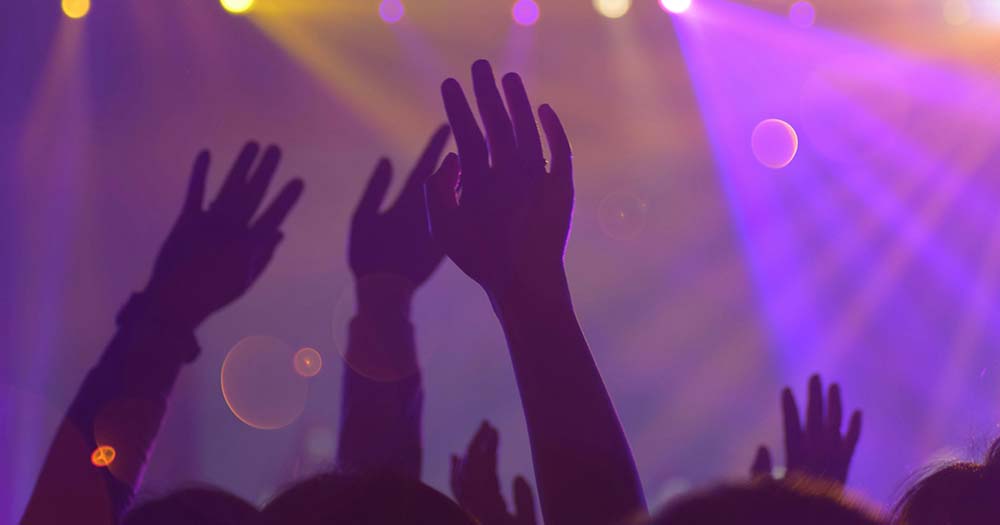 Photo of hands raised in a club setting with purple lighting representing Dublin's upcoming Dyke Night