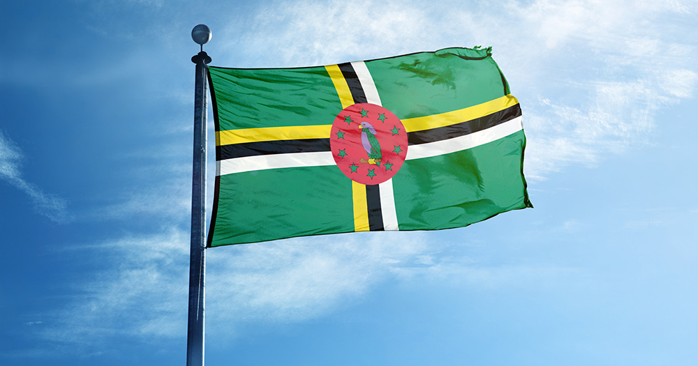 Flag of Dominica, where same-sex activity has been decriminalised. It is a green flag, with a yellow, black and white cross and a red circle in the middle with a bird and green stars.