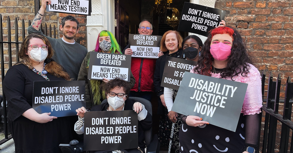 Activists from Irish disability rights groups posing for a photo while holding signs that read 'disability justice now' and 'don't ignore disabled people power'.
