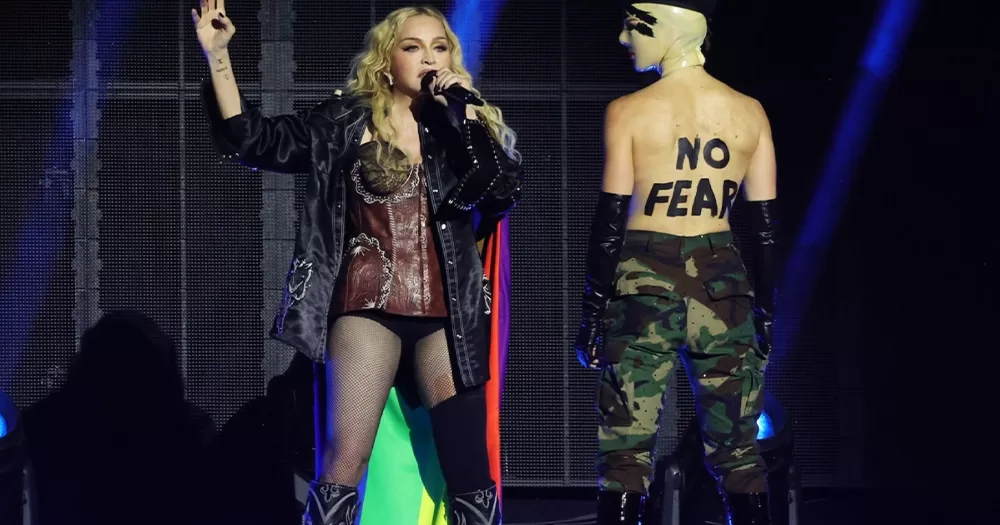 Madonna on stage in Miami, Florida for her Celebration Tour standing beside a shirtless dancer with 'No Fear' written across his back.