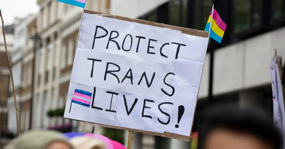 This article is about new NHS gender identity clinics. The image shows a sign reading "Protect trans lives!"