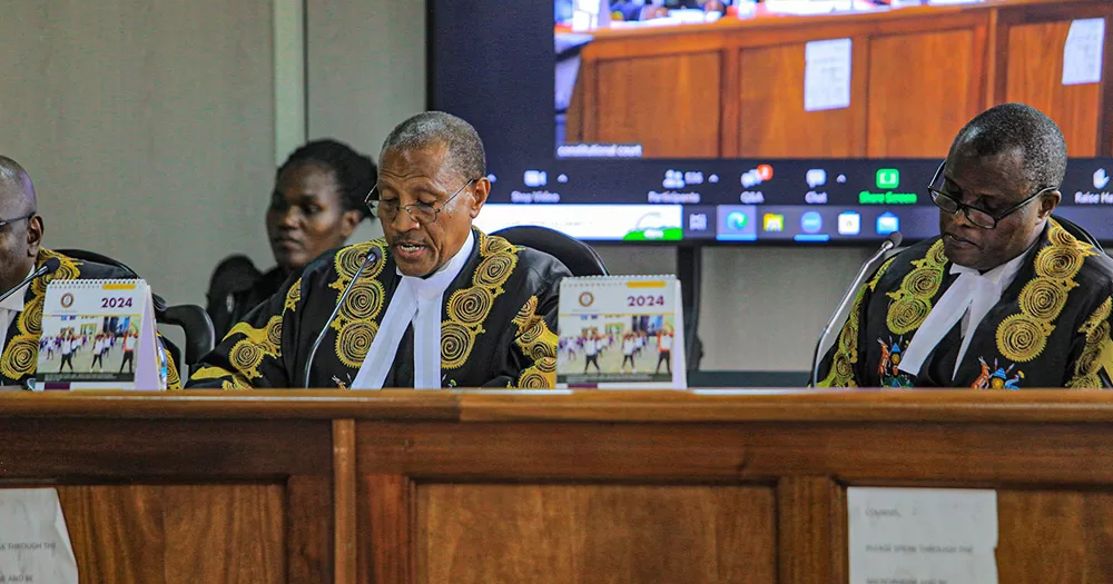 A judge in Uganda delivering a court ruling on the country's anti-LGBTQ+ law. The image shows the judge sitting alongside colleagues at the top of a courtroom. He talks into a microphone.