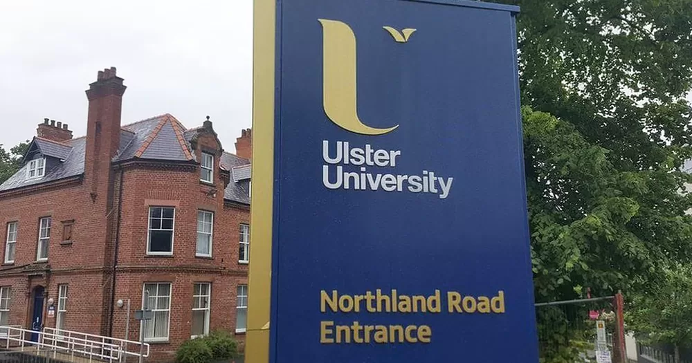 Entrance of Ulster University, which has a partnered campus in Qatar, with a blue and yellow sign and a red-bricks building in the background.