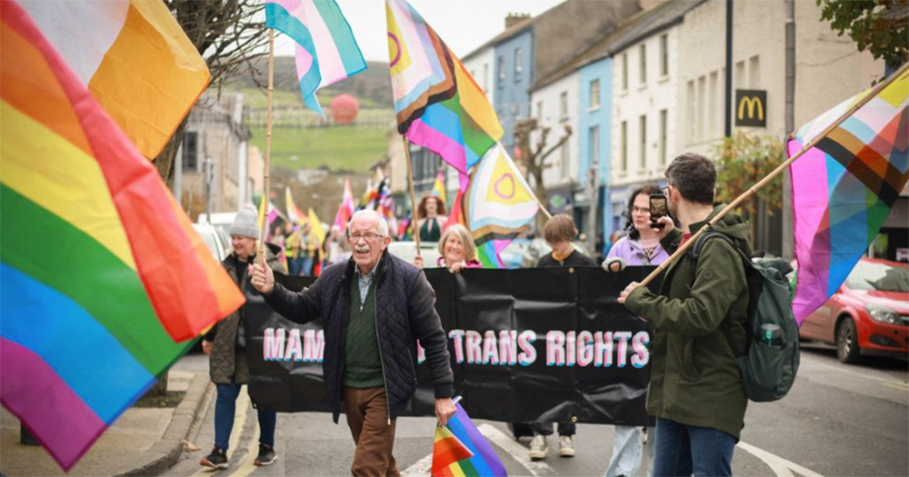An image from the 2023 Pride parade at Clonmel Pride Festival. Lots of rainbow and LGBTQ+ flags are visibile, as an older man walks at the front of the photo, followed by the Mammies for Trans Rights group.