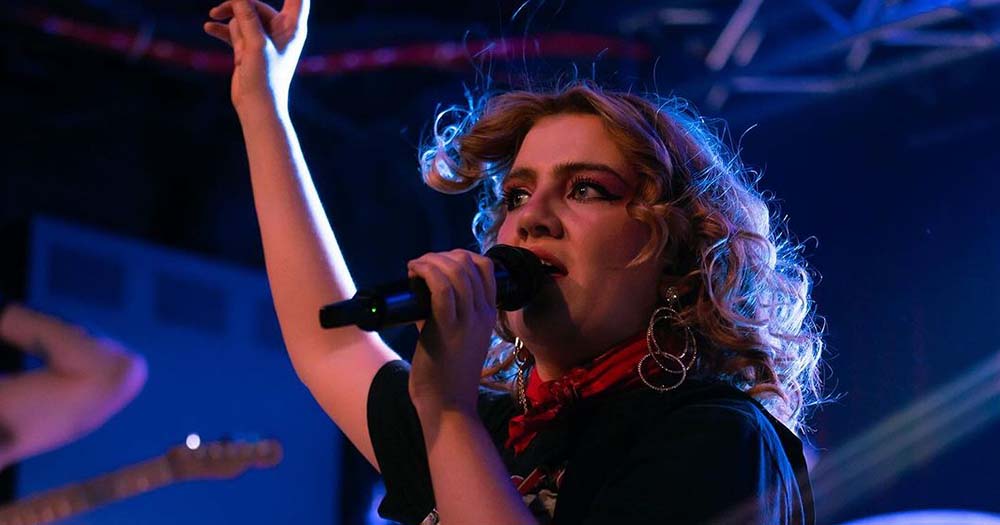 Photo of CMAT performing on stage, she recently pulled out of the Latitude Festival in solidarity with Palestine.