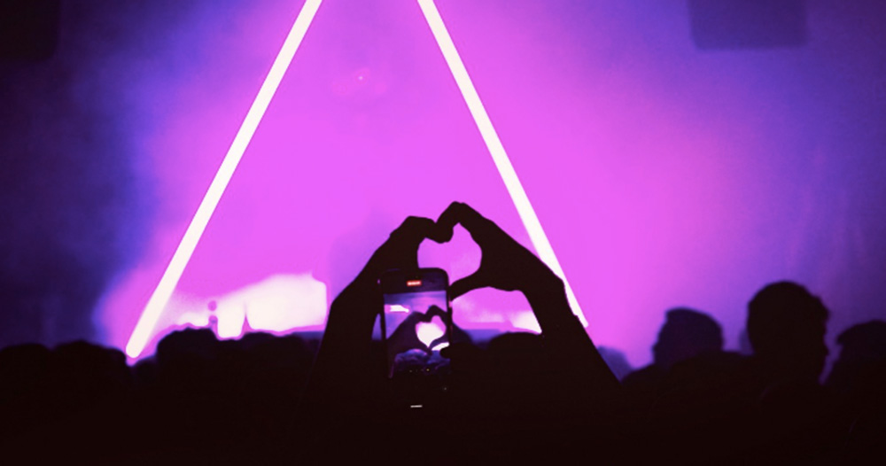 This article is about Mother's A Night For Gaza event. The image shows a silhouette of raised hands making a heart shape in front of a glowing pink triangle in a nightclub.