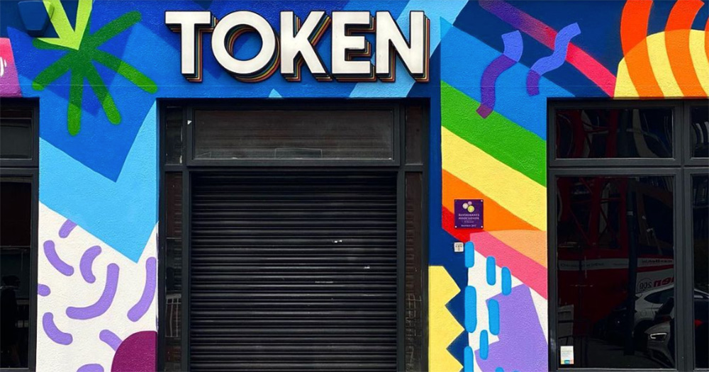 Exterior of Dublin bar Token. The venue's sign is shown in the image, with a colourful mural painted on the wall. The shutters are down on the door.