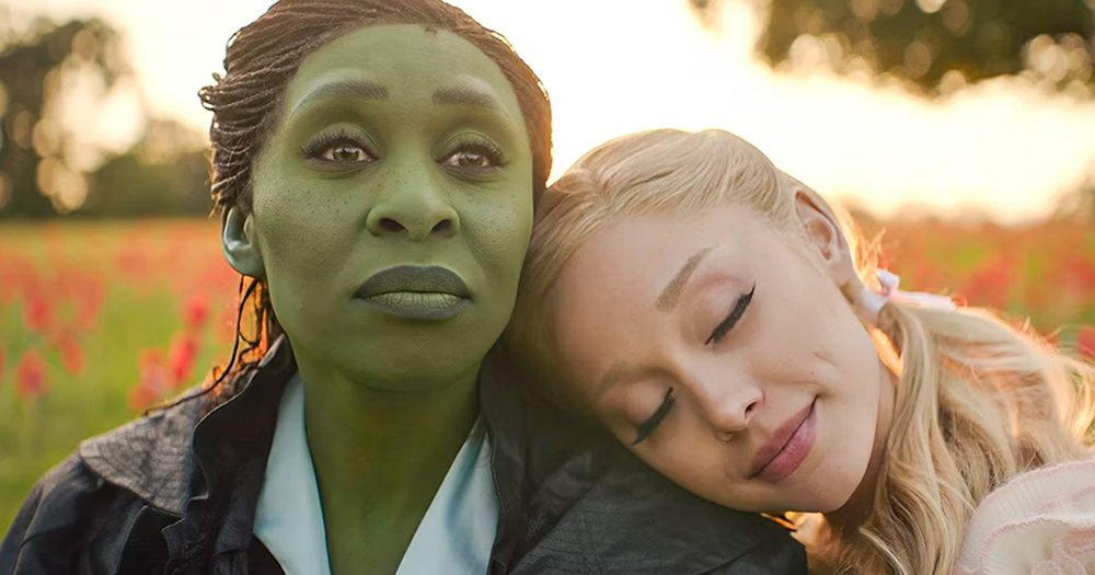 A screencap showing Cynthia Erivo and Ariana Grande as Elphaba and Glinda in 'Wicked: Part One'. Grande leans her head on Erivo's shoulder while the sun sets behind them.