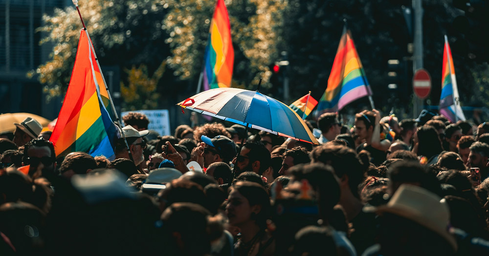 Photograph of people gathering outdoors holding LGBTQ+ Pride flags.