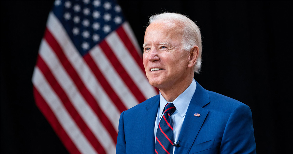 United States president Joe Biden turns to face the left while standing in front of an American flag.