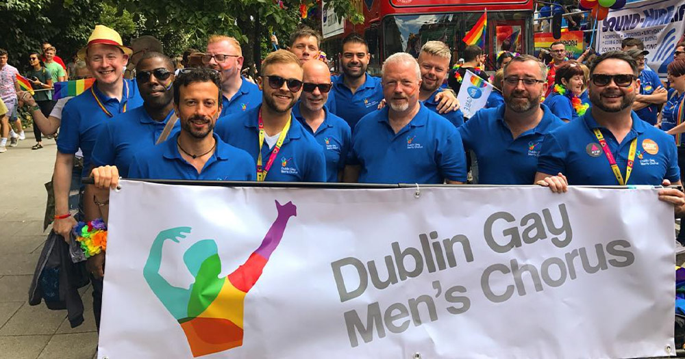 A photograph of the members of the Dublin Gay Men's Chorus holding a banner for the group during a Pride event.
