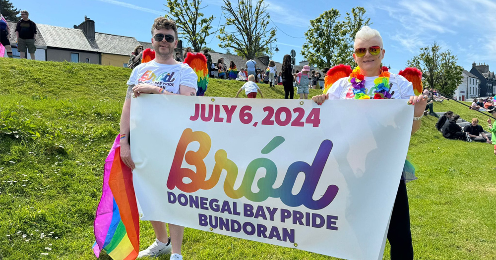 Two members of the Donegal Bay Pride team hold a banner outside that features the group's logo and information about their first parade.