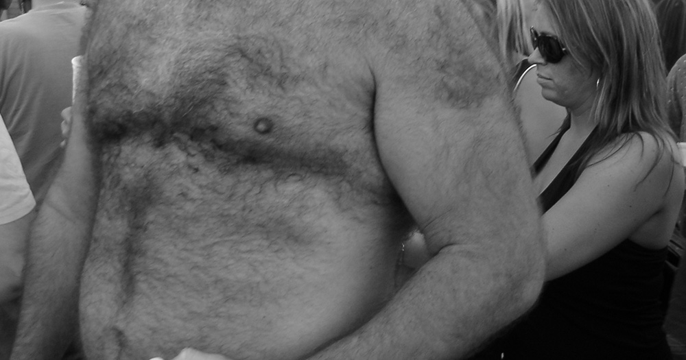 This article is about gay body standards. The image is a black and white photo of a man's torso. He is of a bigger build and has lots of hair on his body.