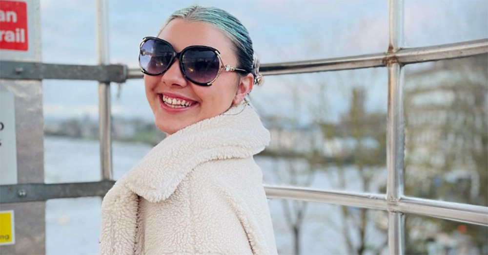 Image of Natasha O'Brien who was attacked by an Irish soldier, Cathal Crotty. She is photographed from the shoulders up, wearing a white coat and sunglasses. She smiles at the camera.