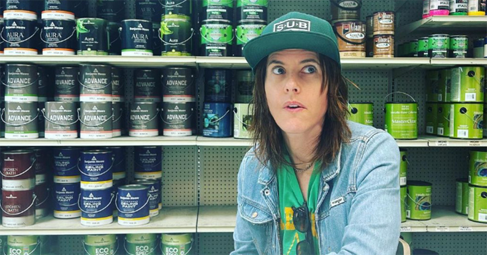 Photo of Kate Moennig, rumoured to star in a new audio erotica, from the chest up wearing a baseball cap. She stands in front of tins of paint in a hardware store.
