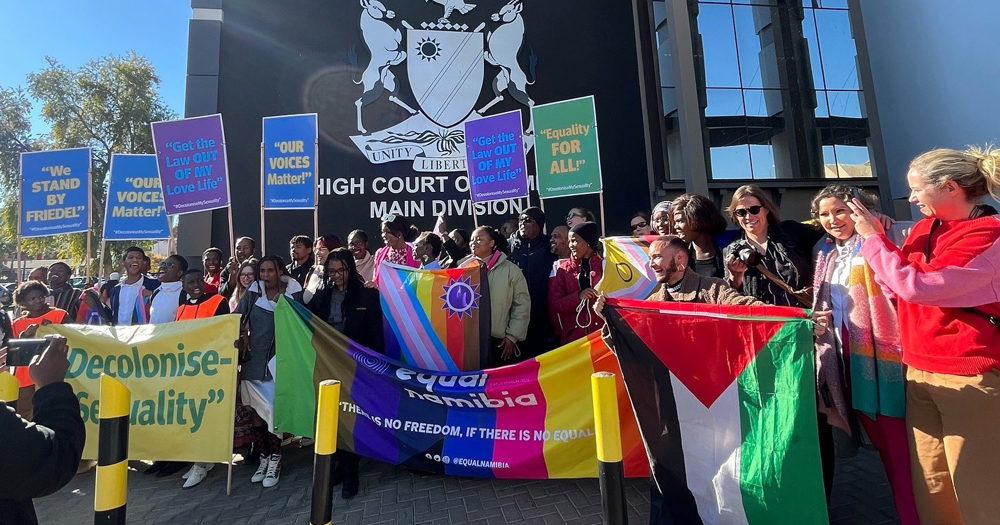 Activists posing outside the High Court in Namibia after a ban on same-sex activity was overturned. They are holding flags and signs with messages of support.