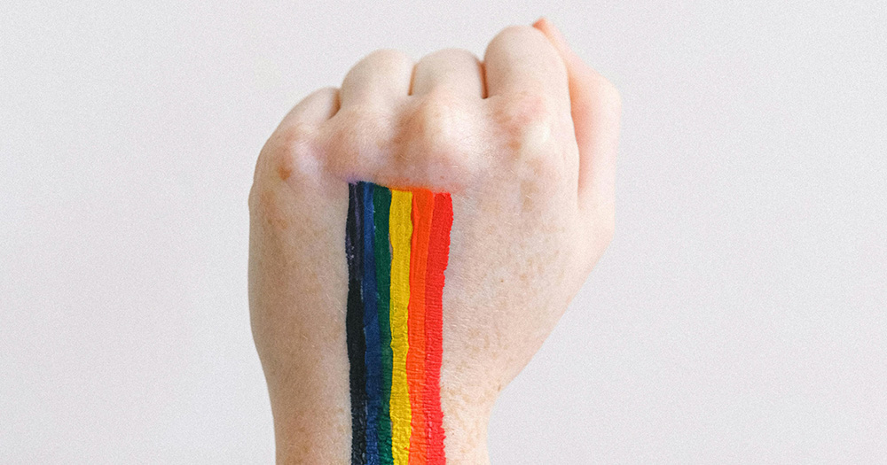 This article is about the National LGBTI+ Inclusion Strategy. The image shows a fist raised, with rainbow colours painted on the hand.