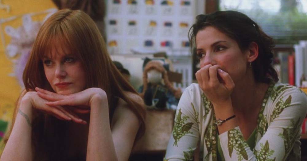 Photo of Sandra Bullock and Nicole Kidman sitting at table in 1998 film, Practical Magic.