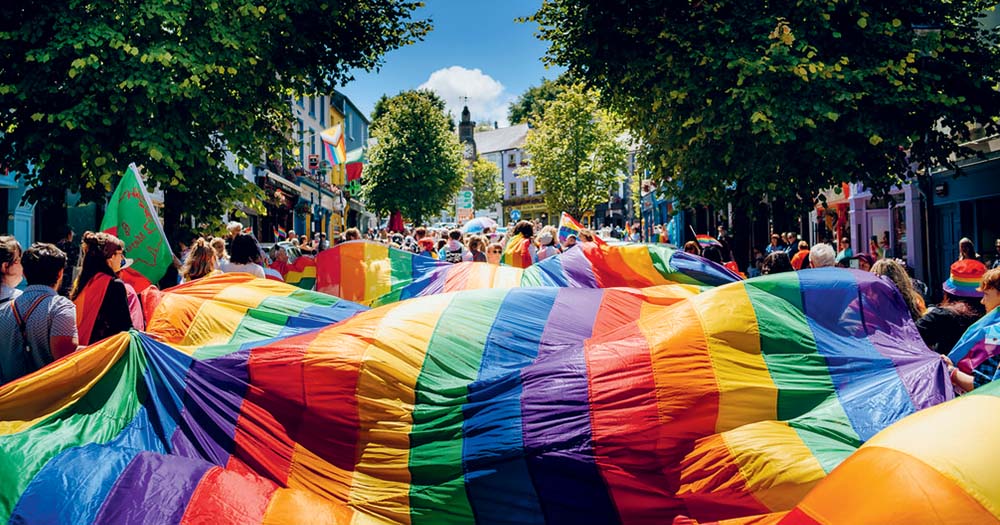 Photo of giant rainbow Pride flag being carried down the street representing Pride season in Ireland