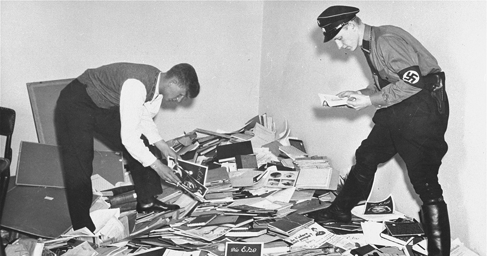 Magnus Hirschfeld's sexology institute is raided by Nazis who burn their documents. The black and white image shows two men, one in a Nazi uniform raiding an office with lots of paper documents on the floor.
