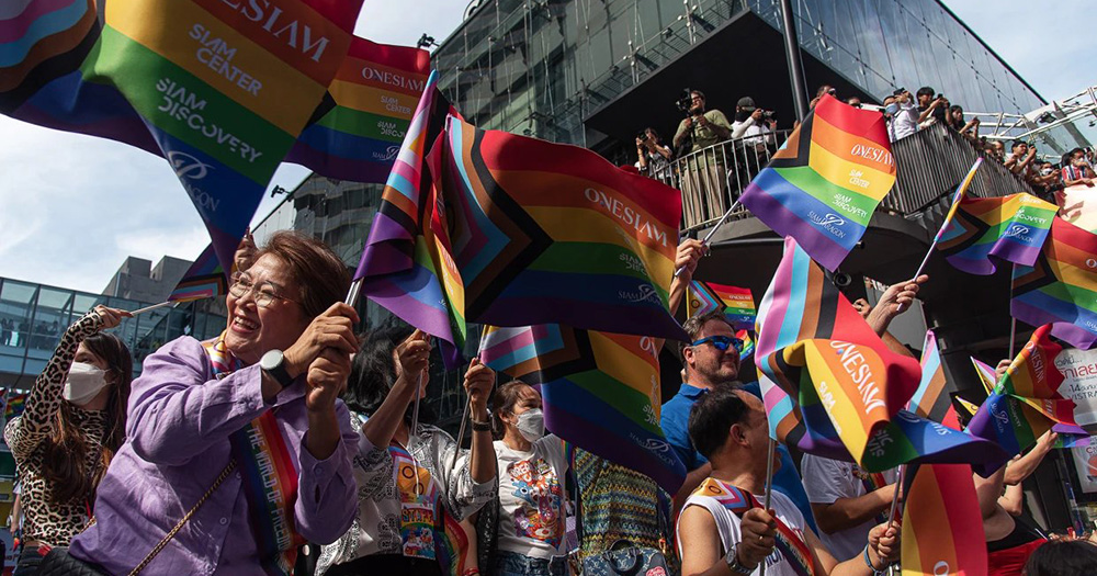 People in Thailand celebrating the legalisation of same-sex marriage. A big group of people fly Pride flags in the streets.