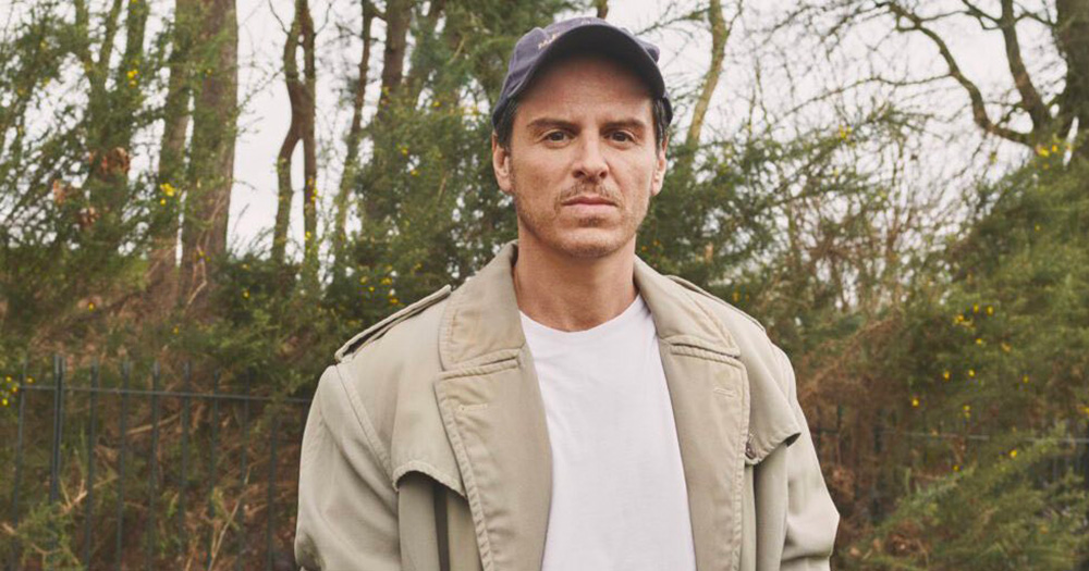 Image of Pressure star Andrew Scott. He is photographed in the outdoors from the chest up, wearing a trench coat, white t-shirt and navy cap.