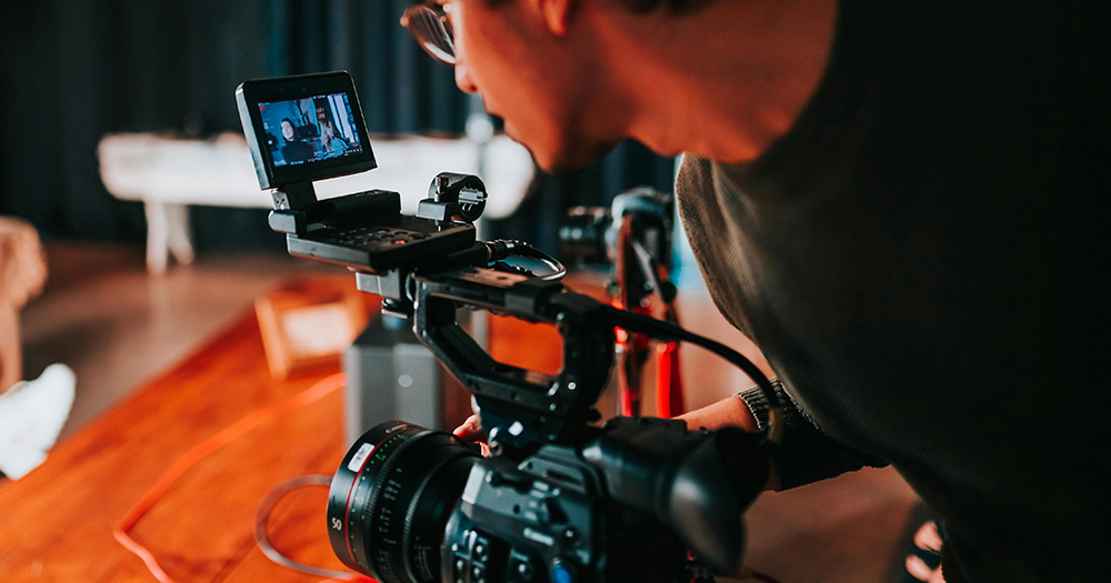 This article is about GAZE's new development scheme. The image shows a filmmaker looking at the screen of a camera.