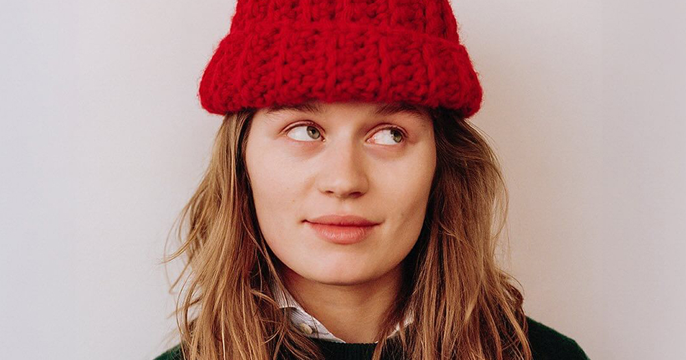 Photo of singer girl in red, who's coming to Dublin at the end of August, looking up and wearing a red beanie.