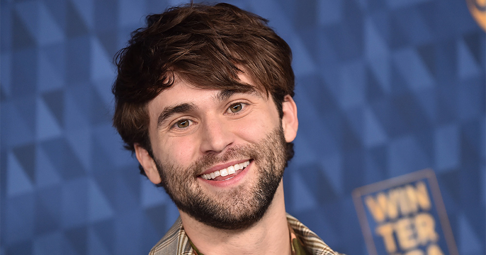Grey's Anatomy actor Jake Borelli hits the red carpet and smiles for a photo.