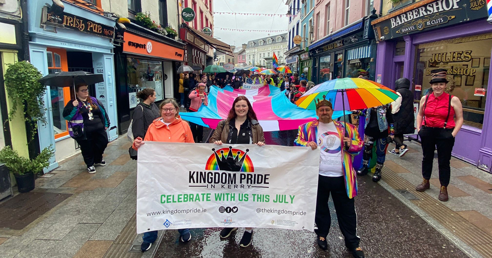 People marching with a banner that reads 'Kingdom Pride, carrying a big trans flag.