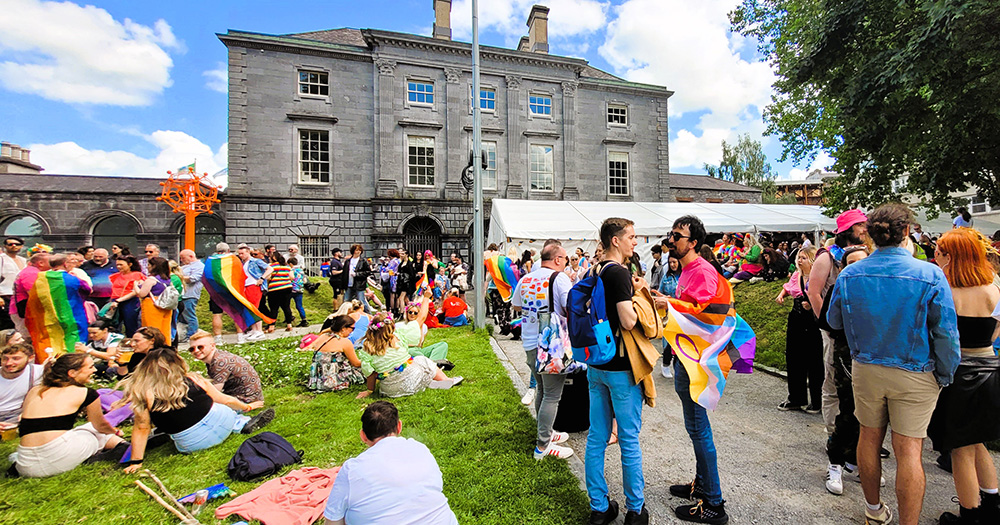Image from the Limerick Pride launch. It shows a group of people with rainbow flags socialising in the gardens of a museum.