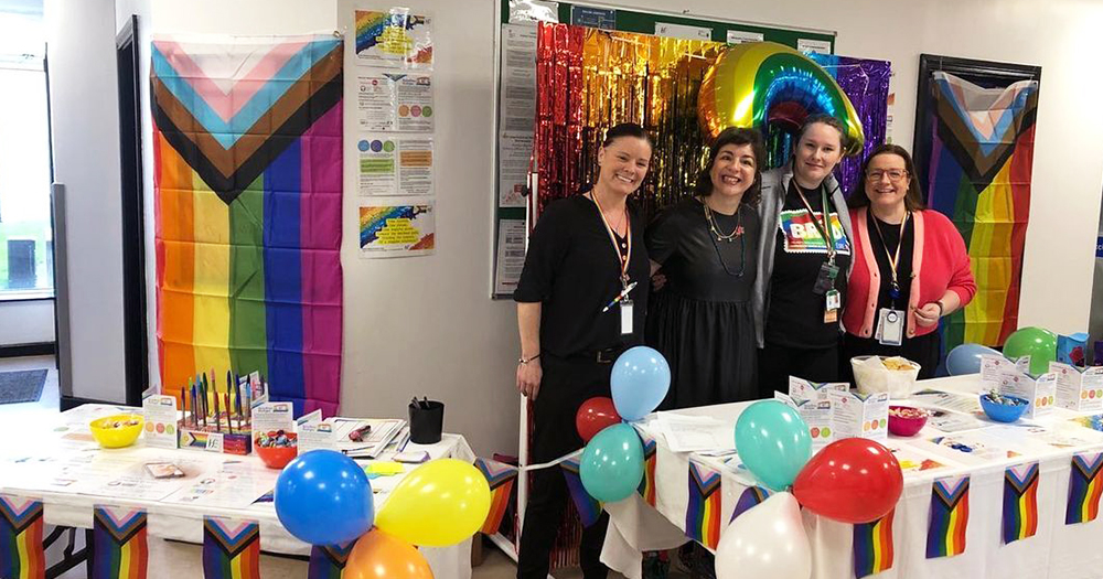 Photo of organisers of Mullingar Pride festival posing behind a table in a room full of rainbow decorations.
