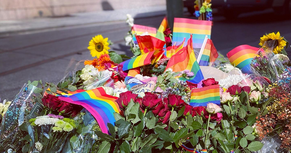 Photo of a pile of rainbow flags and flowers, a tribute to the two lives lost as a result of the shooting at Olso Pride in 2022.