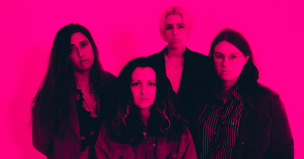 Promotional photo of Pillow Queens for their upcoming Irish national tour. The band is photographed in heavy pink light.