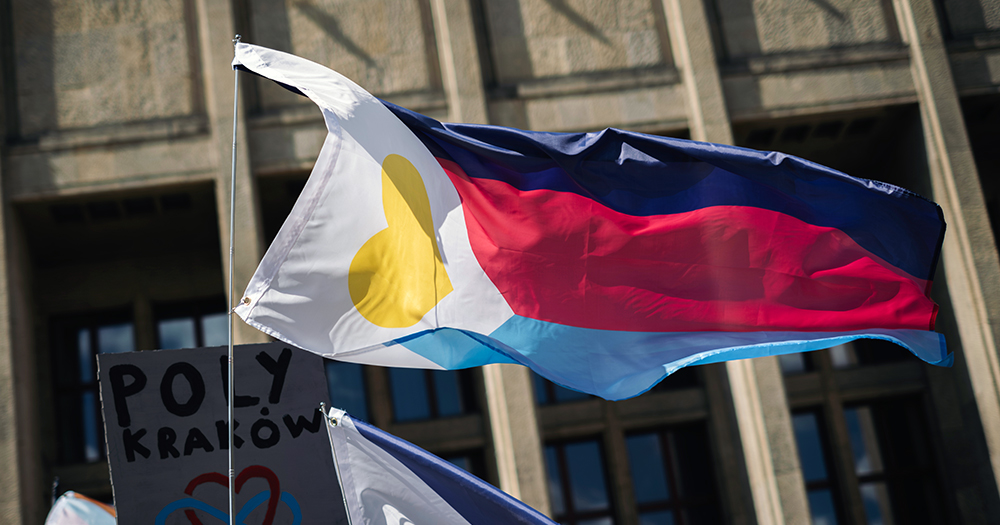 The polyamory Pride flag blowing in the wind, with a yellow heart on a white triangle and three blue, red and light blue stripes.