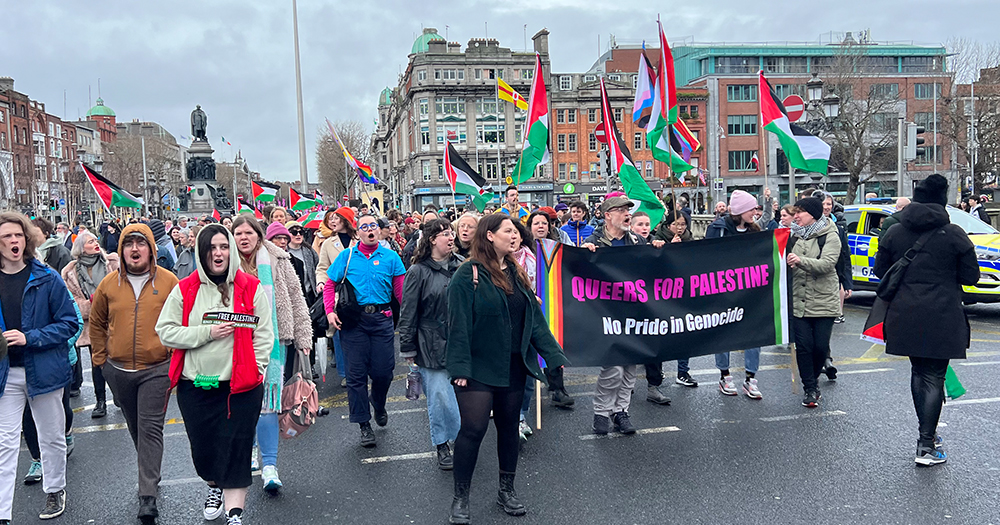 Photo of Queers for Palestine group marching in Dublin with a big banner and Pride and Palestinians flags.