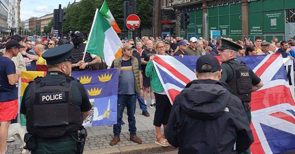 Anti-immigration ralliers in Belfast hold Irish and UK flags as police look on.