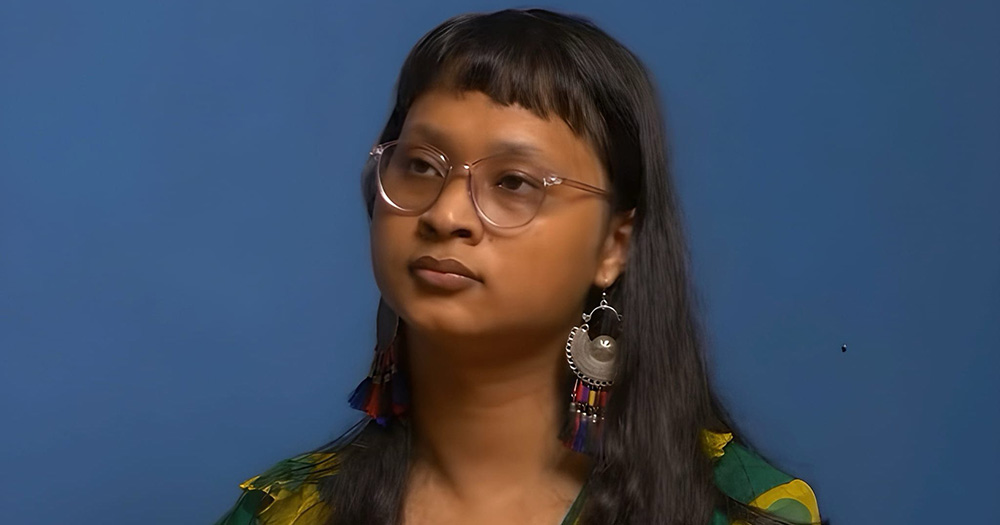 A photo of a transgender woman from Nepal. She is photographed from the shoulders up, looking slightly into the distance in front of a blue background.