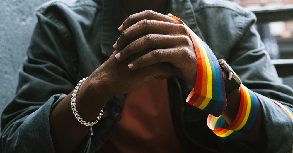 This article is about Ireland's disregard legislation. The image shows a close up of a person's hands clasped together with a rainbow ribbon wrapped around one of the hands.