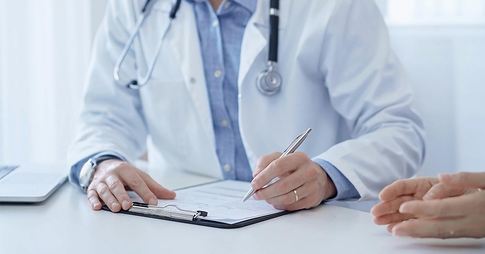 This article is about guidelines for the medical care of intersex children in Ireland. In the photo, the hands of a doctor writing on a medical chart while sitting at a desk.