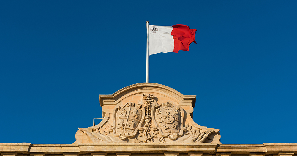 This article is about Malta introducing non-binary gender markers for official documents. In the photo, the Maltese flag flying on top of a building.