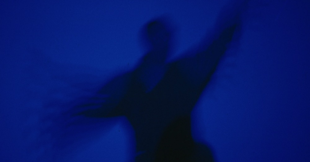 Photo of live performance show Blue Now, showing a person in dark blue light dancing.