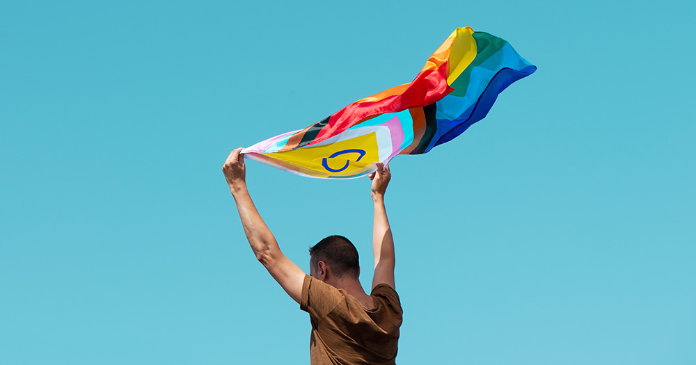 This article is about the hate crime bill passing the Dáil. The image shows a man holding a Pride Progress flag above his head.