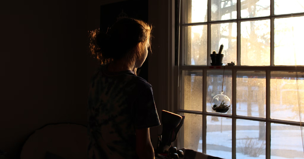 This article is about domestic abuse in queer relationships. In the photo, a woman looking out a window.