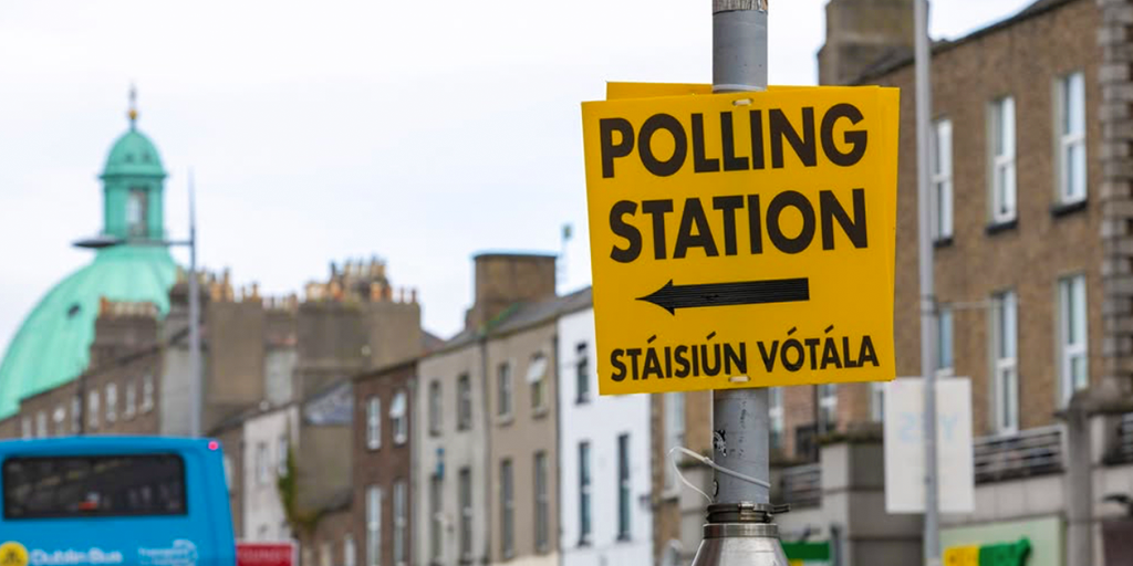 This article covers the political party general election manifestos. The image shows a yellow sign directing towards a polling station.